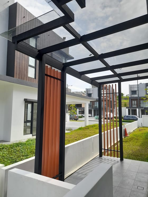 从下方仰望一座已完工的玻璃屋顶，架在黑色钢构上，覆盖新建排屋的车道，一侧是木纹直立格栅，玻璃之外是晴朗的天空。